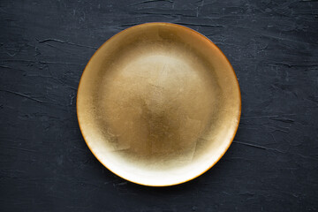 Empty golden plate on black background, top view. Diet or cooking concept. 