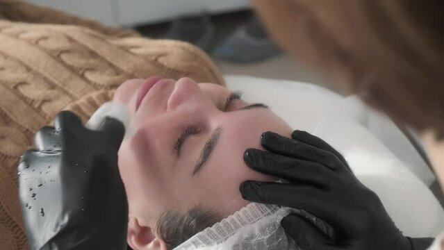 Profile portrait of relaxed woman's face, cosmetologist removes skincare product