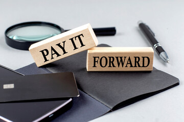 PAY IT FORWARD text on wooden block on black notebook , business concept