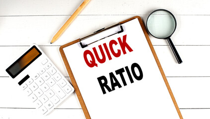 QUICK RATIO words on clipboard, with calculator, magnifier and pencil on the white wooden background