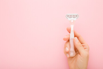 Young adult woman hand holding razor on light pink table background. Pastel color. Closeup. Female product for smooth body skin. Empty place for text. Top down view.