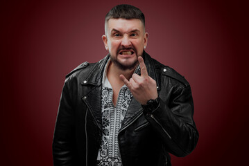 The man is dressed in a Ukrainian shirt; a man in a leather jacket poses on a red background; shows different facial expressions and gestures; poses in sunglasses in the studio; charismatic portrait o