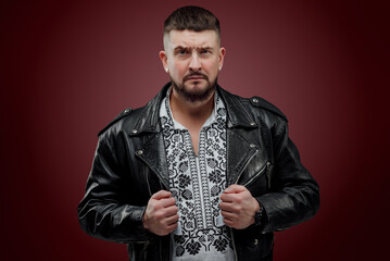 The man is dressed in a Ukrainian shirt; a man in a leather jacket poses on a red background; shows...