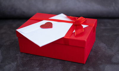 Romantic love letter in white envelope with Valentines heart and gift box with red ribbon on gray sofa. Happy Valentine's Day concept