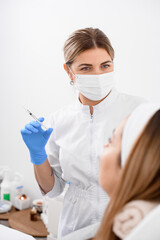 professional female doctor in mask with gloves on her hands holds a syringe with liquid