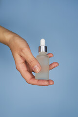 Female hands with serum in bottles on blue background