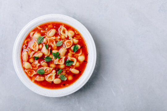 Tomato soup. Minestrone soup. Tomato bean and pasta soup bowl on gray stone background.