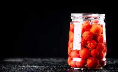 Pickled tomatoes in a glass jar on the table. 
