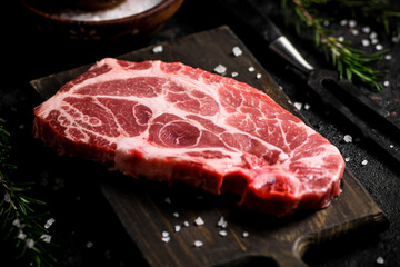 Raw pork steak on a cutting board with spices and rosemary. 