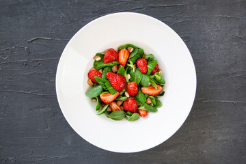 Tasty summer strawberry salad in white plate on black background, top view. Healthy diet dish. 