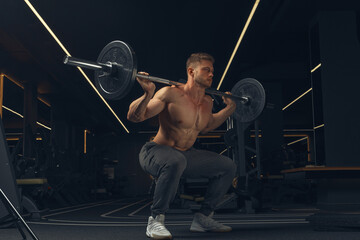 Muscular man doing squats with barbell in a gym. Male bodybuilder doing workout Confident young man...
