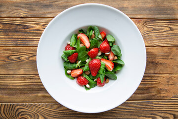 Tasty summer strawberry salad on wooden rustic table, top view. Healthy diet dish. 
