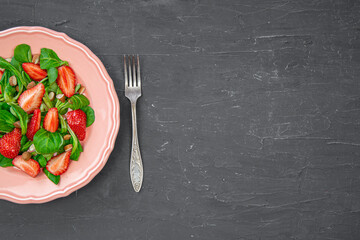 Tasty healthy summer salad with strawberry, fork cutlery and space for text, copy space, black marble background, top view. 