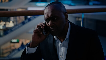 Pensive senior ethnic businessman sad answer call displeased talking mobile phone African American upset frustrated businessman talk with smartphone indoors stressed middle-aged man business problem