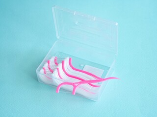 Dental floss with a plastic toothpick in white and pink in a plastic transparent container on blue. Dental concept