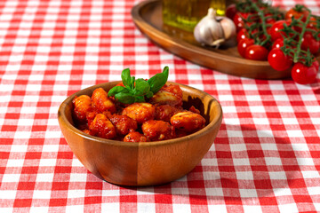 gnocchi with tomatoes and basil in a wooden bowl on a red checkered tablecloth