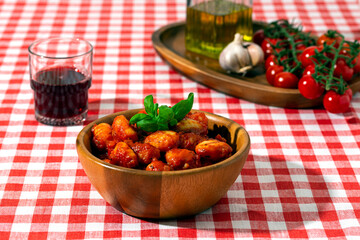 gnocchi with tomatoes and basil in a wooden bowl on a red checkered tablecloth