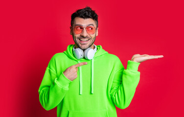 Happy man presenting product isolated on red. Fashion man pointing finger studio