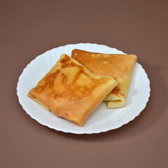 Two ruddy fresh square pancakes on a white plate, on a brown background