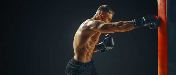Strong muscular man punching a bag with boxing gloves. Isolated Free copy space. Sportsman kick...