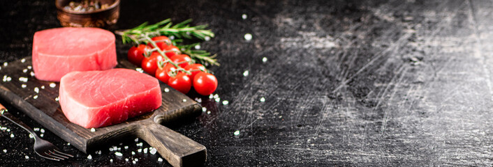 Fresh raw tuna on a cutting board with tomatoes, spices and rosemary. 