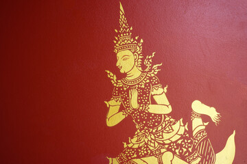 The ancient drawing on the wall of the temple. The painting of the angle in the gold color on the red background