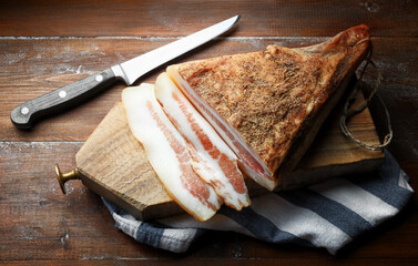 Guanciale, bacon, with cutting board and knife on wooden background, close-up.