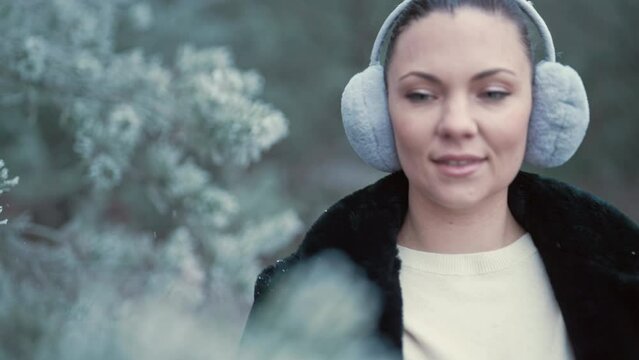 Stylish woman in fluffy ear muffs walking in winter frozen forest. Enjoy nature.
