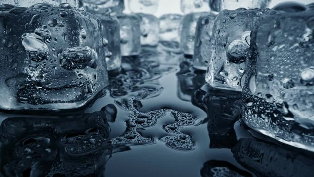 Melted ice cubes close up. Camera moves through ice cubes with water drops over dark background. Wet melted ice cubes with waterdrops. Ice super macro. Slider shot, 4K UHD