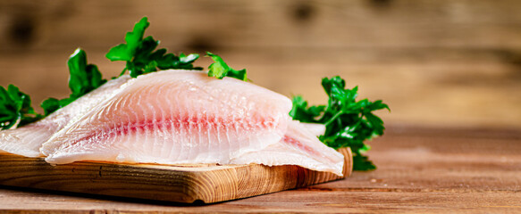 Raw fish fillet with parsley on a cutting board. 