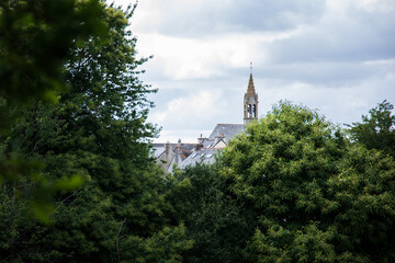 Fototapeta na wymiar Photographie du clocher d'un village de campagne derrière des arbres. Il s'agit du village de Mellionnec, en Centre-Bretagne. 