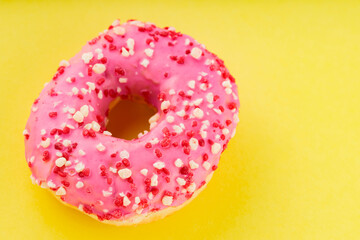Sweet pink donut with multicolored sprinkles on yellow background. Colorful sweet dessert