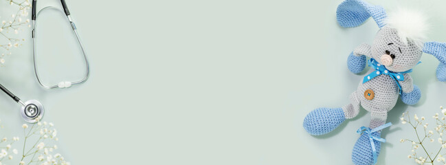 Kids health care banner. Cute knitted toy rabbit with a stethoscope on blue background with white flowers. Family doctor or pediatrician concept. Banner size. Copy space for text