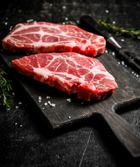 Raw pork steak on a cutting board with rosemary. 