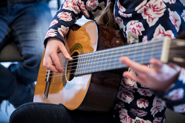 Photographie des mains d'une élève dans un cours de musique grattant les cordes de sa guitare.