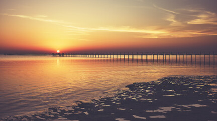 Seascape with a wooden pier silhouette at sunset, color toning applied.