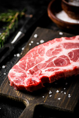 Raw pork steak on a cutting board with spices and rosemary. 