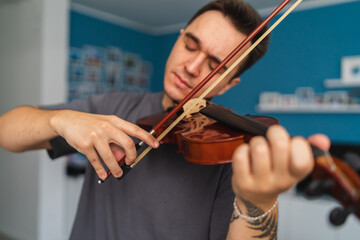 A portrait of a young guy playing or learning a violin in his home private classes online course for violin music © Dusan