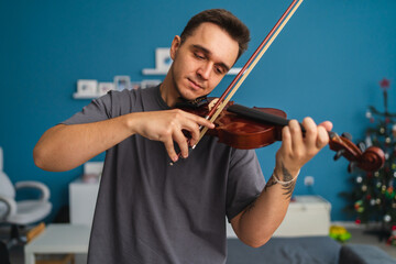 A portrait of a young guy playing or learning a violin in his home private classes online course for violin music
