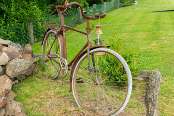 Sweden, Knislinge – July 5, 2022: Old rusty worn out bicycle in a yard of private house as a decoration. Unusual sculpture, concept, idea.