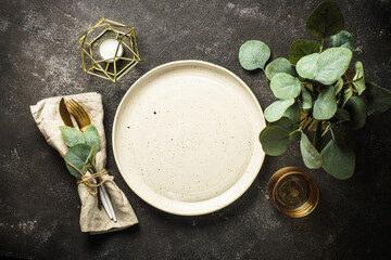 Table setting with white craft plate, cutlery and decorations at black stone table. Top view image.