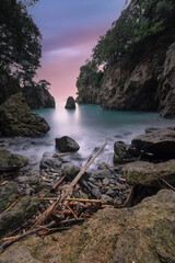 Fototapeta na wymiar Pink sunset over the sea with lonely rock in an Italian cove