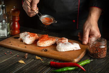 Professional cook adds paprika to chicken wings. Raw chicken wing in the kitchen of a restaurant or...