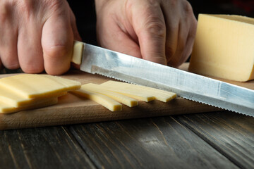 Close-up of a chef hands with a knife slicing cheese on a cutting board in a restaurant kitchen. Preparing dairy food for breakfast while on a diet