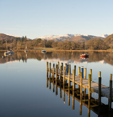 Beautiful Morning at Ambleside Pier.  Perfect reflections on lake Windermere, boats and snowy mountains in the background