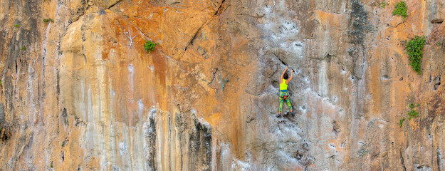 A woman climber climbs a mountain along a steep cliff. The athlete climbs a vertical stone wall...