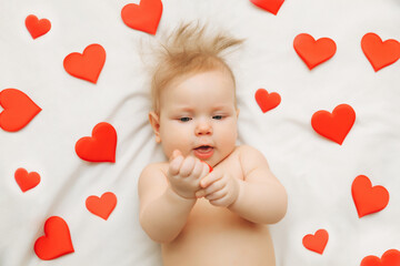 the baby is 6 months old lying on the bed among hearts , the concept of love and Valentine's Day.