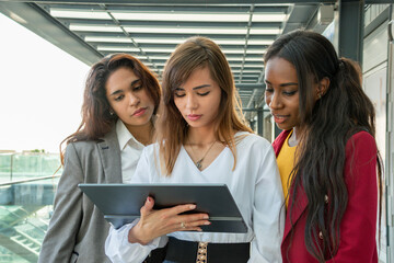 Three attractive businesswomen monitor the progress of their business with the tablet at their...