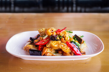 Thai-style stir-fried chicken with cashew Nuts, popular Thai food, served in plate on wooden table.