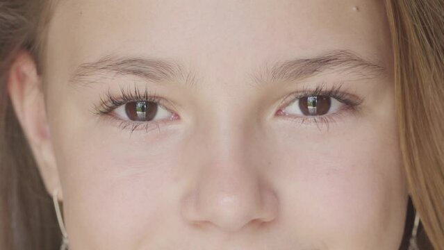 Beautiful brown eyes of teen smiling girl looking at camera. Macro view of attractive happy face with opened eyes. Cropped closeup